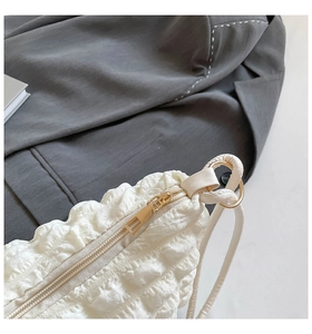 Detail of white pleated fabric shoulder bag featuring gold zipper and metal hardware