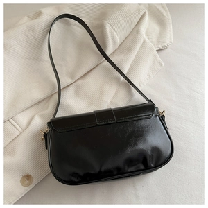 Détail du sac sous l'aisselle en noir brillant avec boucle dorée et texture en cuir