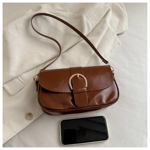 Gros plan d'un sac bandoulière en cuir marron avec boucle dorée sur fond de tissu blanc
