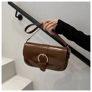Détail d'un sac en cuir verni marron foncé avec boucle dorée sur escalier blanc