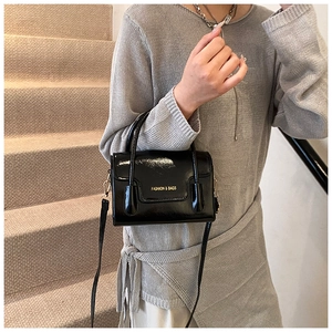 Detailed view of black patent leather square handbag with gold hardware and strap