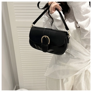 Détail d'un sac à bandoulière noir avec boucle dorée en mors de cheval sur le rabat