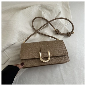 Close-up of woven texture brown shoulder bag with golden horseshoe buckle on corduroy