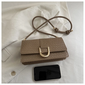 Detail view of woven texture handbag with golden U-buckle and smartphone for scale
