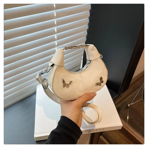 Détail d'un sac demi-lune beige avec charmes papillon argentés et boucle métallique
