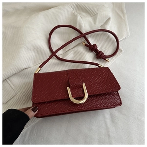 Close-up of wine red woven leather handbag with gold U-shaped metal lock on knit fabric