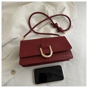 Detailed close-up of woven wine red leather bag with golden U-buckle and smartphone for scale
