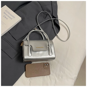 Close-up of textured silver square bag with gold metal hardware and brand engraving