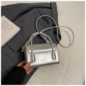 Détail du sac bandoulière argenté à texture métallique et accents dorés sur un costume