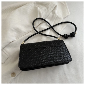 Macro detail of black woven texture handbag with gold metal hardware and knotted strap