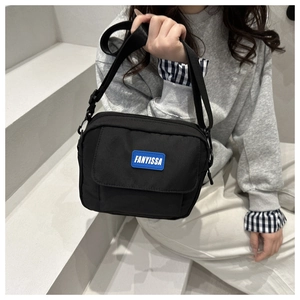 Detail of black crossbody bag with blue rubber logo and adjustable woven shoulder strap