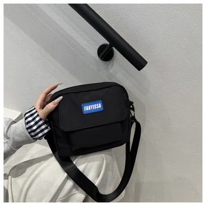 Détail de la sacoche noire en nylon avec bandoulière réglable et étiquette bleue logo