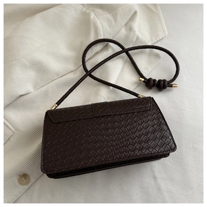 Detail of dark brown embossed leather handbag with woven shoulder strap and gold accents