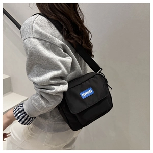Detail of black crossbody bag with blue FANYISSA logo patch worn by a model