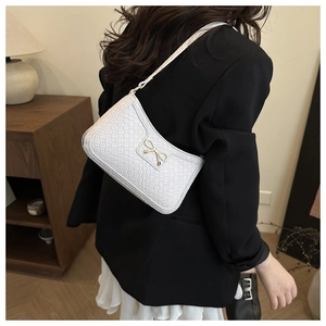 Close-up of white woven shoulder bag featuring a metallic gold bow buckle detail
