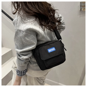 Detail of black nylon crossbody bag featuring a distinctive blue silicone logo patch
