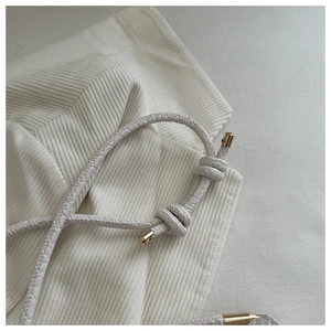 Detail of white woven leather strap featuring adjustable knots and gold metal end caps