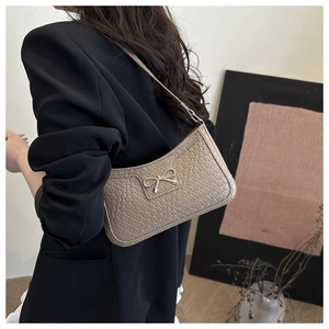 Detail of khaki croc-embossed underarm bag with silver bow ornament on black blazer