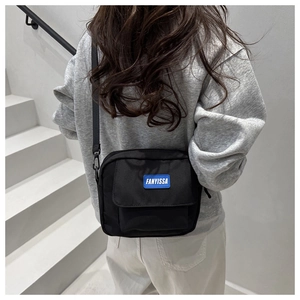 Model wearing a black nylon crossbody bag with blue logo patch and adjustable strap