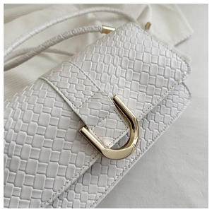 Close-up of white woven leather texture and golden U-shaped buckle on a bag