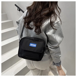 Detail of a black nylon crossbody bag featuring a blue brand label and adjustable strap