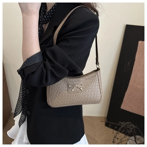 Detail of beige woven underarm bag featuring a delicate gold bow metal fastener