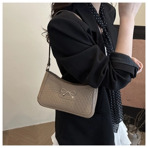 Close-up of khaki shoulder bag with woven texture and a metallic bow detail on the front