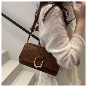 Detail of woven brown leather shoulder bag with gold horseshoe buckle and knot strap