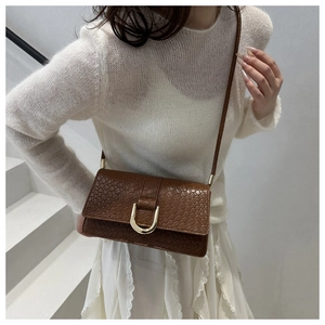 Detail of a brown crocodile pattern bag with a gold U-shaped buckle on a model