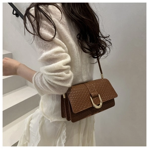Brown woven texture handbag detail with gold horseshoe clasp shown on a model