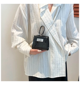 Primer plano de mini bolso bandolera de charol negro con cierre y cadena plateada
