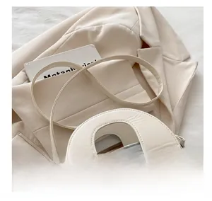 Detail view of silver shell bag with wide cream top handle on neutral background