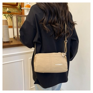 Model wearing a beige waterproof nylon crossbody bag in a cozy cafe setting