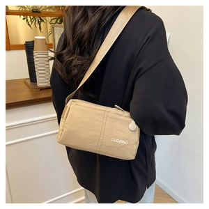 Close-up of khaki nylon crossbody bag with logo detail worn by a model in a cafe