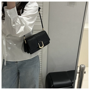 Detail of black textured leather bag with gold U-shaped buckle and metal hardware