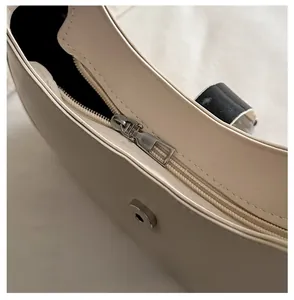 Detail of smooth silver zipper and magnetic snap closure on beige leather shoulder bag
