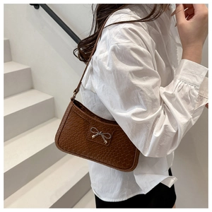 Close-up of brown woven underarm bag featuring a metallic silver bow accent
