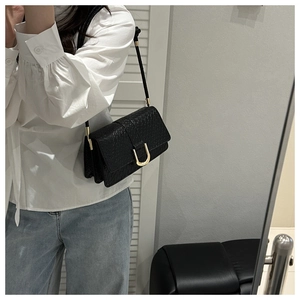 Detail of woven leather texture and gold horseshoe buckle on black shoulder bag