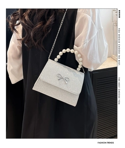 Detail of silver sequin handbag featuring pearl handle and metallic bow accent