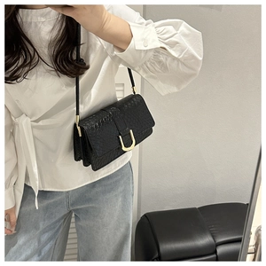 Detail of a black woven leather shoulder bag featuring a prominent gold U-shaped metal buckle