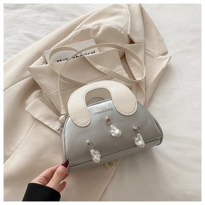 Detail of silver shell bag with metallic leather and unique pearl charms on bed