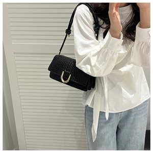 Detail of black woven leather shoulder bag with golden horseshoe buckle and knot strap