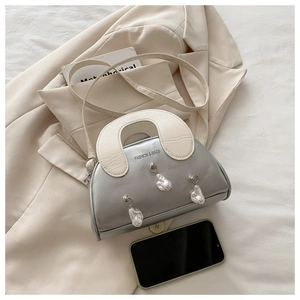Detailed view of silver shell bag featuring irregular pearl charms and cream top handle