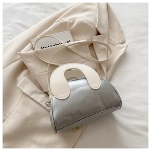 Detail of silver half-moon bag with cream handles on a beige blazer background
