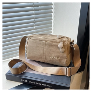 Khaki nylon crossbody bag with multi-layer zippers and adjustable strap on a book