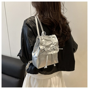 Rear view of a silver metallic pleated backpack with drawstring double bow detail on model