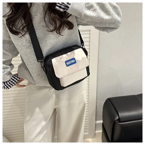 Detail of a minimalist black and white crossbody bag featuring a woven logo patch