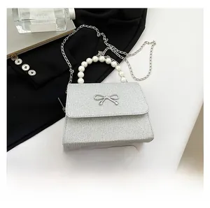 Silver glitter evening bag with pearl handle and metal bow, shown next to a smartphone