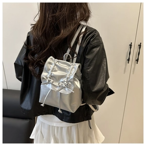 Detail of silver metallic mini backpack with bow accents and drawstring flap design