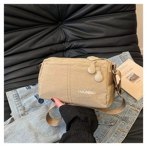 Detail of khaki nylon crossbody bag showing three spherical zippers and brand logo